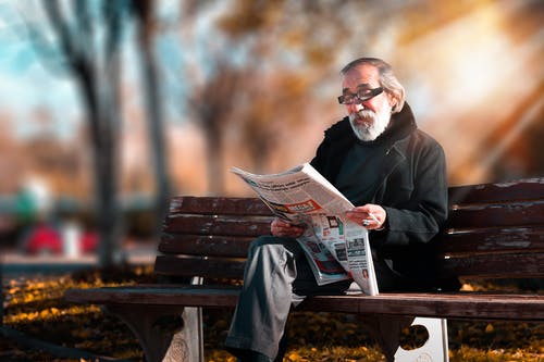 man reading news paper on bench